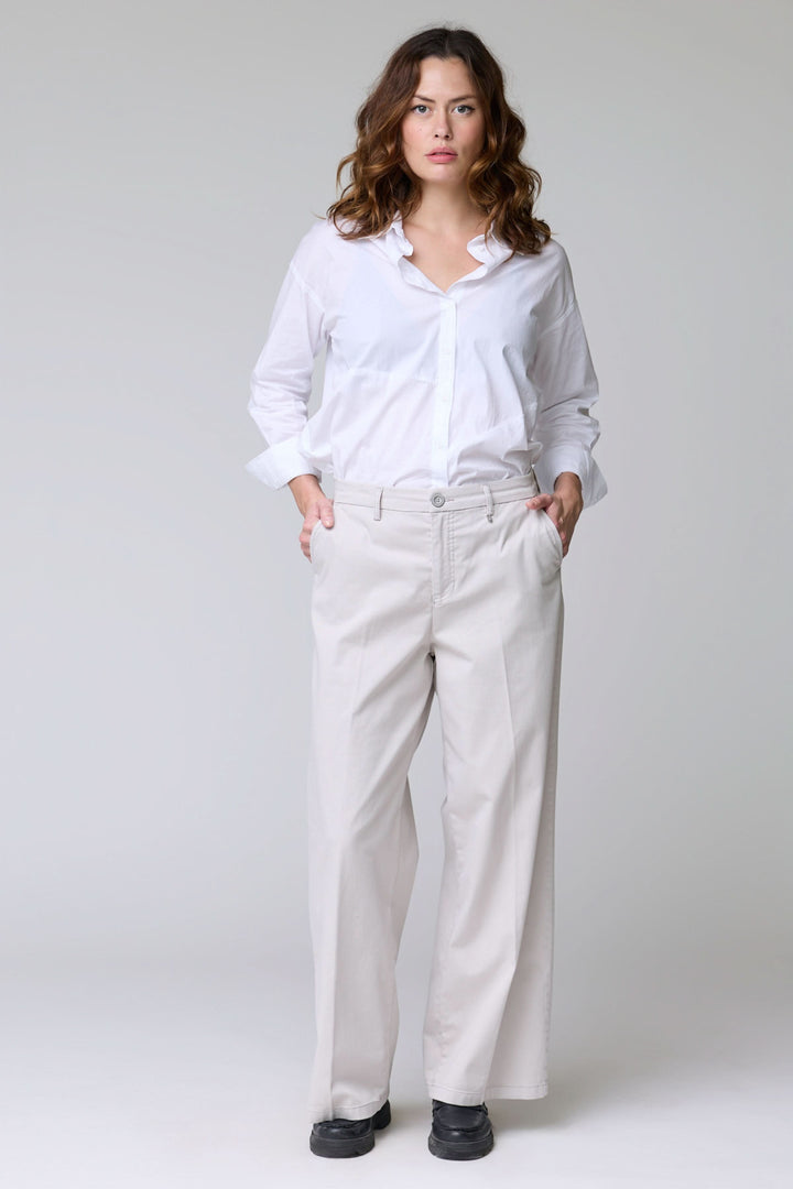 Femme portant un pantalon à jambe large blanc, debout avec une chemise blanche élégante.