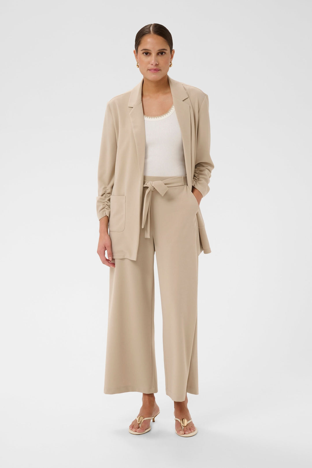 Femme portant Pantalon jambe large Phoebe beige avec ceinture nouée, tenue élégante et polyvalente pour bureau et week-end.