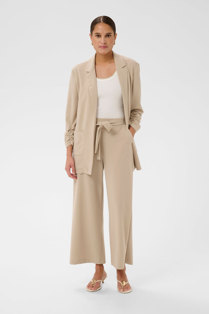 Femme portant Pantalon jambe large Phoebe beige avec ceinture nouée, tenue élégante et polyvalente pour bureau et week-end.