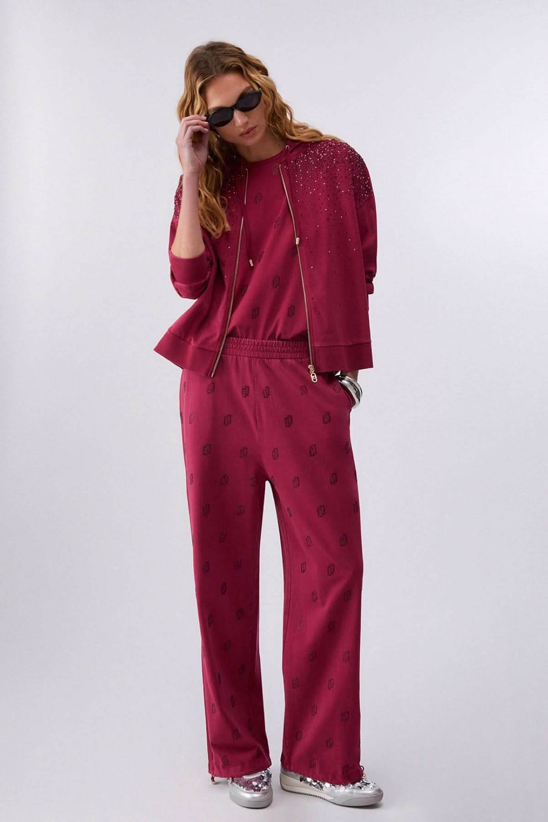 Pantalon jogging imprimé à jambe large avec motif distinctif et taille élastique, style décontracté et moderne, femme portant des lunettes de soleil.