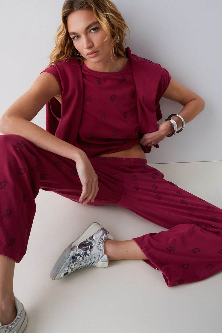 Femme portant un pantalon jogging imprimé à jambe large, silhouette décontractée, motif distinctif, couleur bordeaux et tissu confortable.