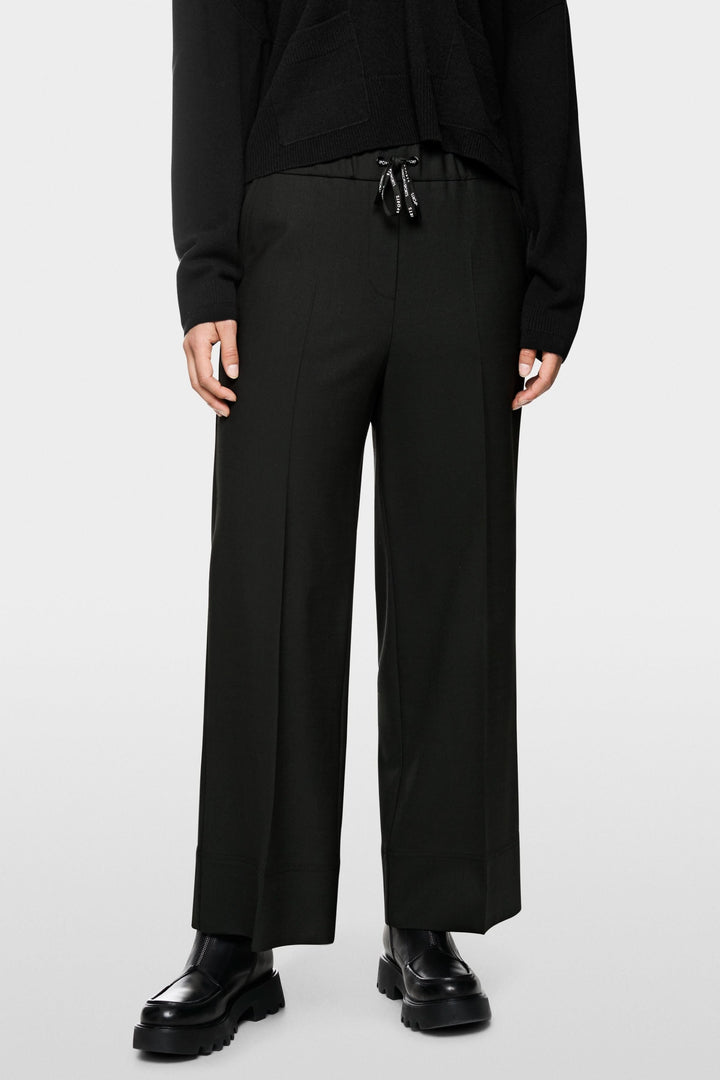 Pantalon large noir, taille élastique avec cordon, porté avec chaussures chunky. Élégance contemporaine et confort décontracté.