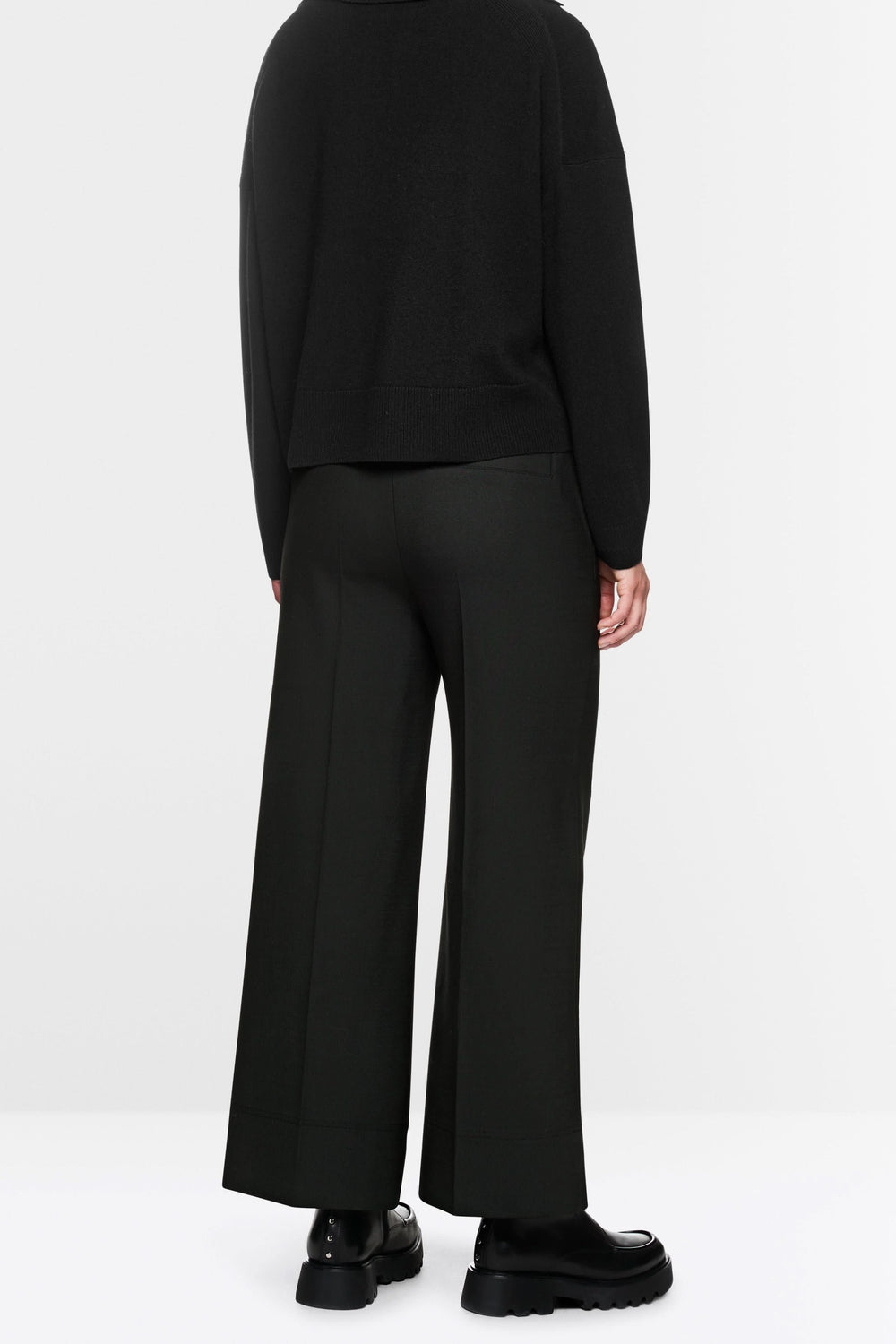 Pantalon large noir avec coupe fluide, élastique et cordon de serrage, porté avec pull ample et chaussures chunky pour look décontracté.
