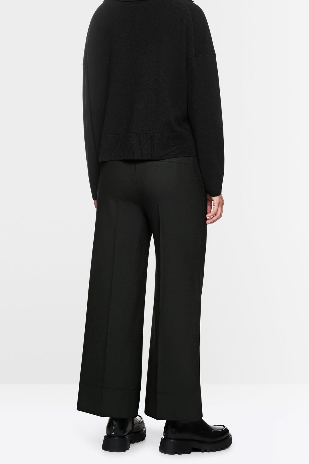Pantalon large noir avec coupe fluide, élastique et cordon de serrage, porté avec pull ample et chaussures chunky pour look décontracté.