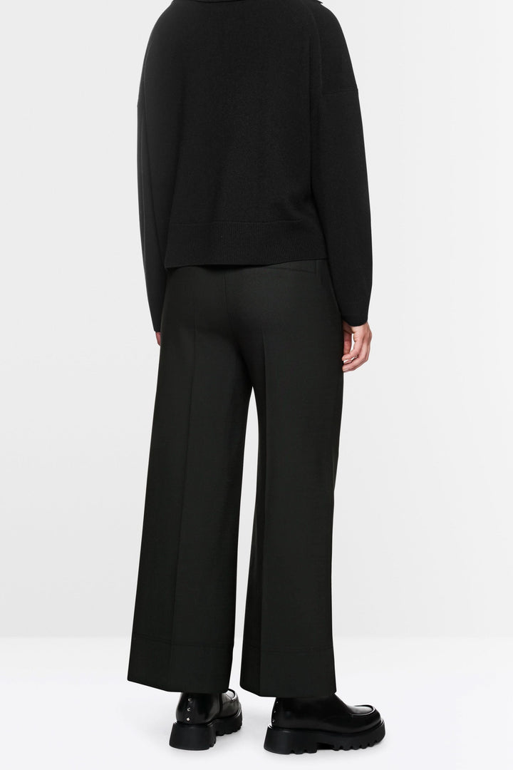 Pantalon large noir avec coupe fluide, élastique et cordon de serrage, porté avec pull ample et chaussures chunky pour look décontracté.