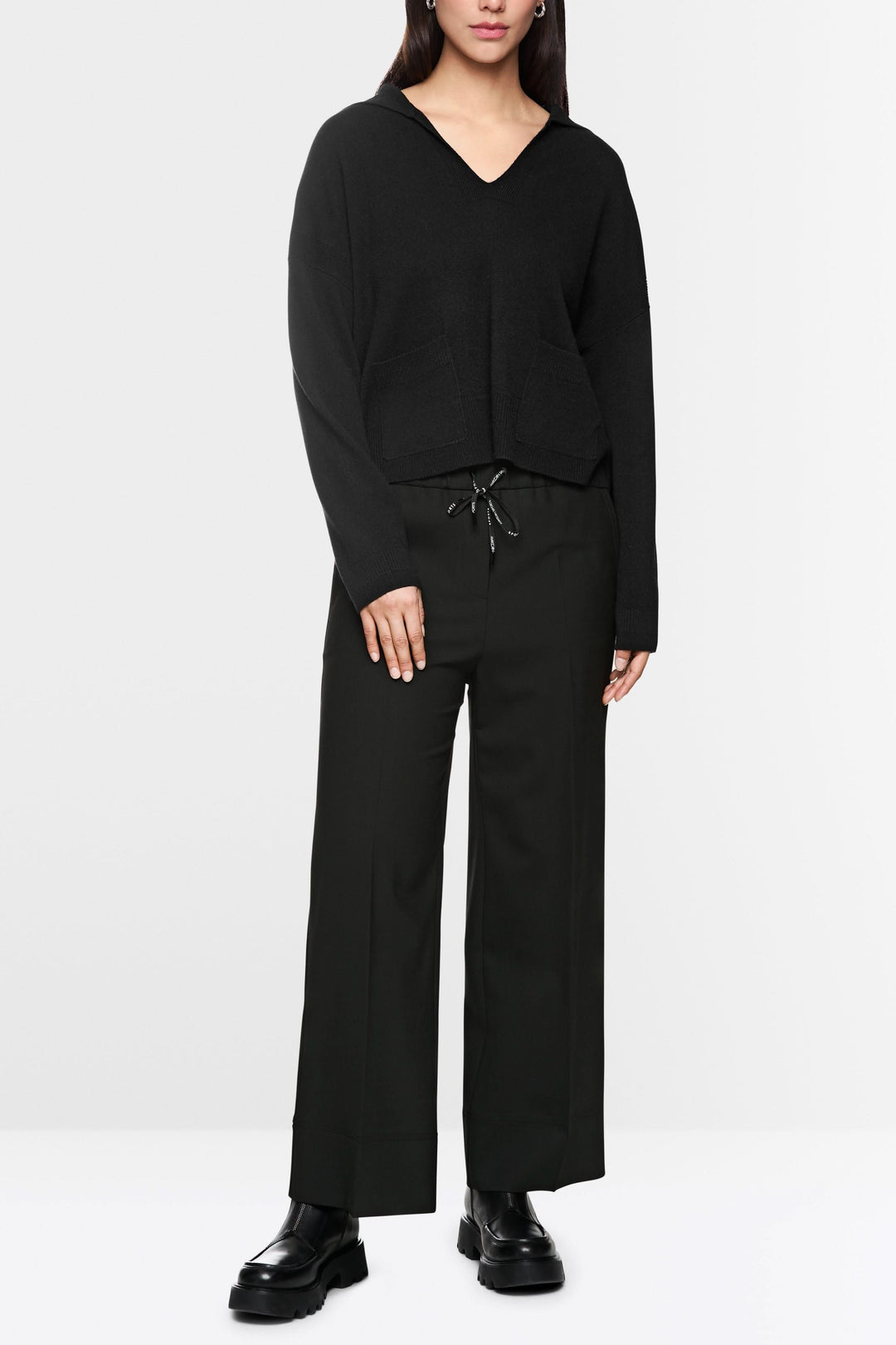 Femme portant un pantalon large noir avec taille élastique et cordon, assorti à un chandail ample noir et des chaussures chunky.