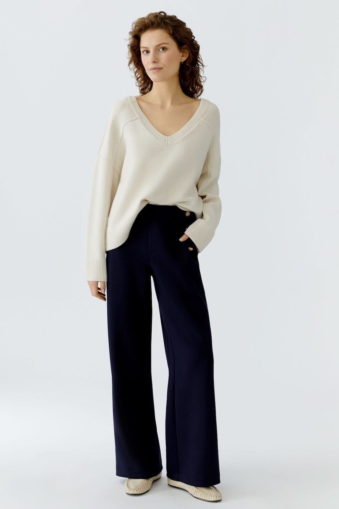 Femme portant un pantalon large à boutons décoratifs et un pull, silhouette élégante et moderne.