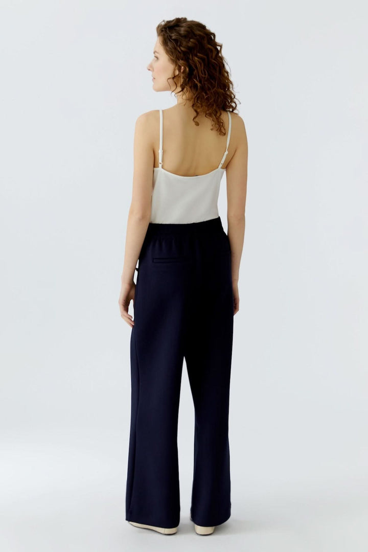 Femme de dos portant un pantalon large à boutons décoratifs avec coupe large et fluide, idéal pour un look sophistiqué et moderne.