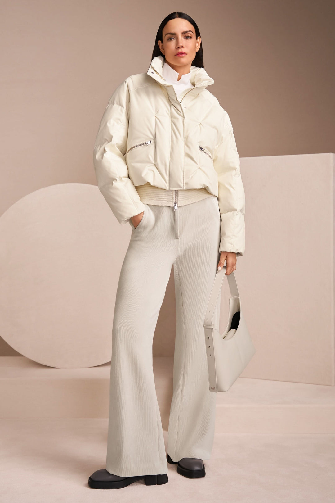 Femme portant un pantalon large en velours côtelé avec une veste blanche matelassée et un sac à main élégant.