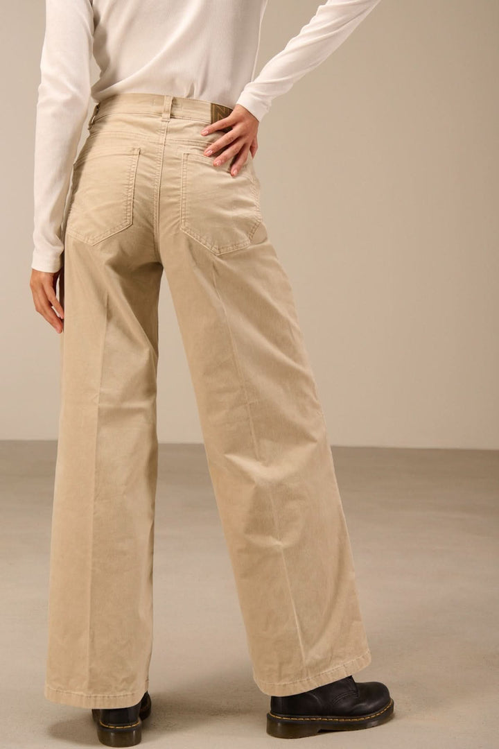 Pantalon large taille haute en velours beige, porté par une personne, vue de dos, montrant la coupe évasée et les poches arrière.
