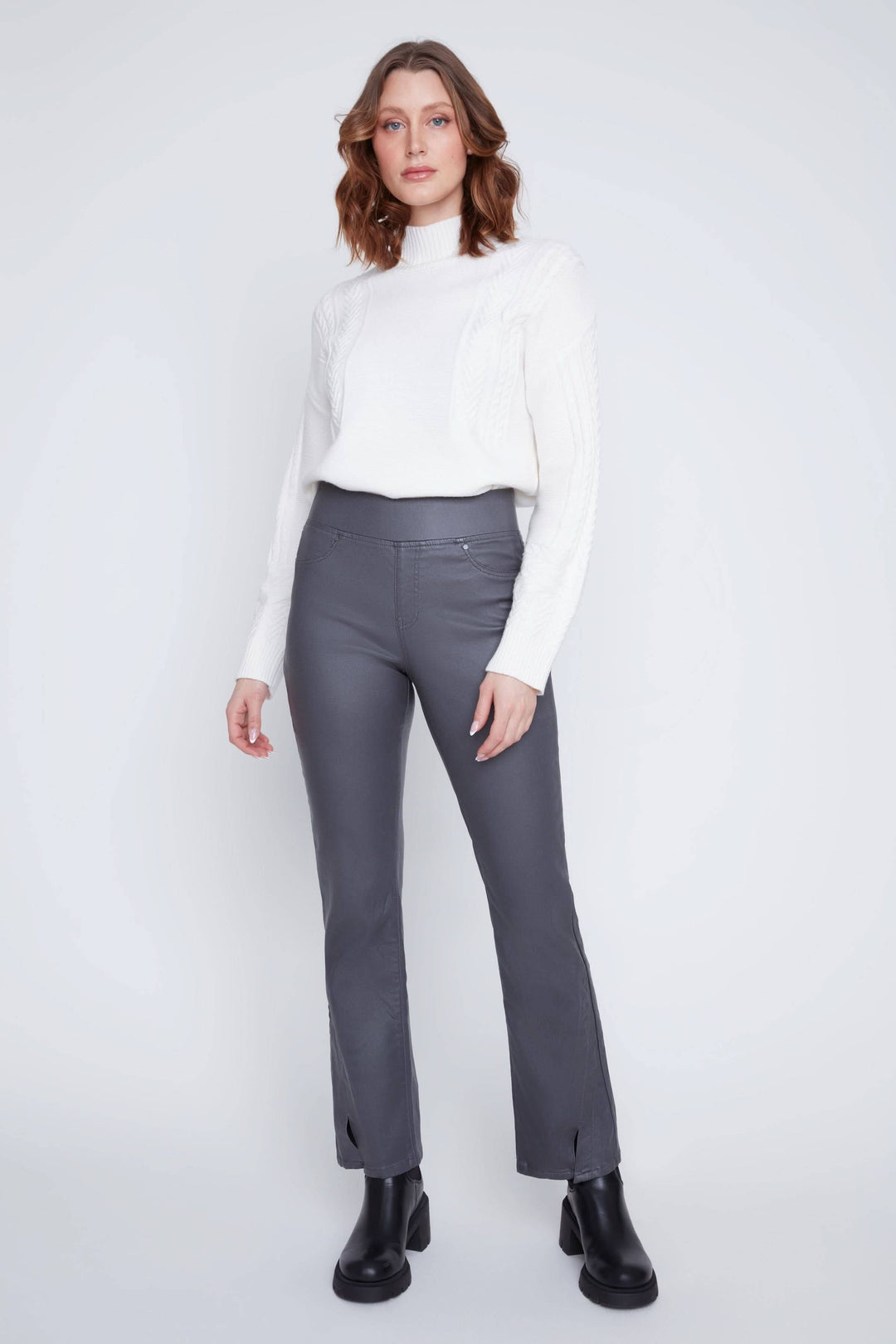 Femme portant un pantalon taille haute gris, ajusté avec fentes aux chevilles, associé à un chandail blanc.