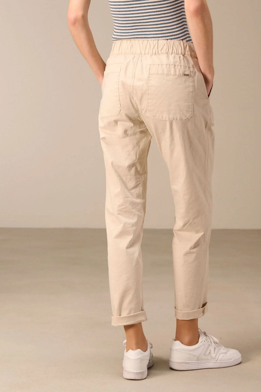 Pantalon taille élastique beige avec coupe droite et cordon ajustable, porté avec des baskets blanches pour un look décontracté.