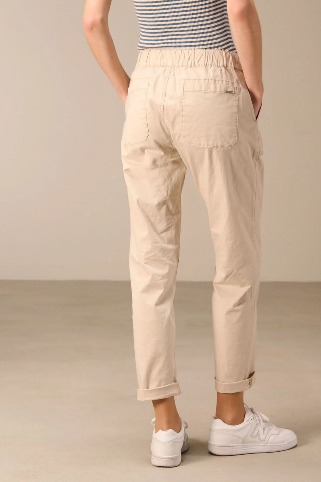 Pantalon taille élastique beige avec coupe droite et cordon ajustable, porté avec des baskets blanches pour un look décontracté.