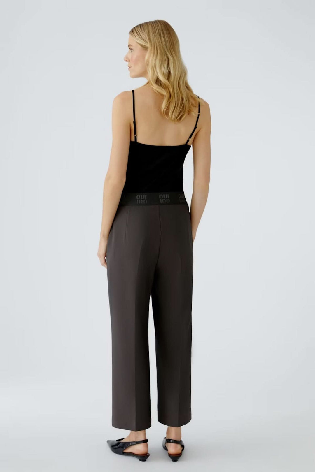 Femme portant un pantalon à taille élastique et coupe ample avec plis marqués, vue de dos, ambiance moderne et élégante.