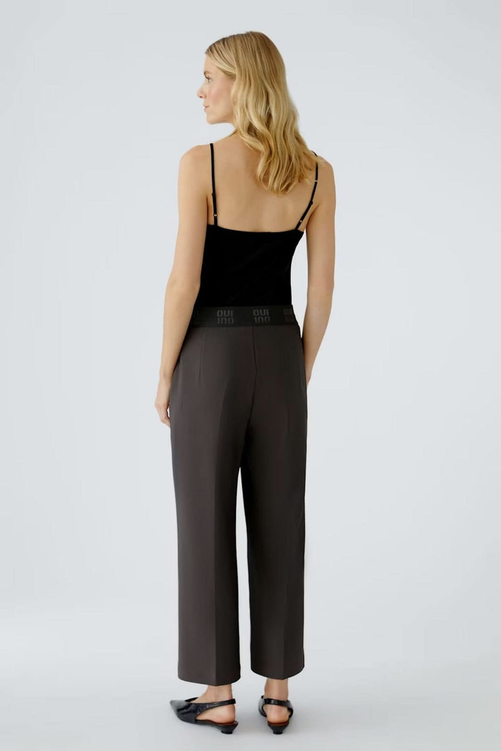 Femme portant un pantalon à taille élastique et coupe ample avec plis marqués, vue de dos, ambiance moderne et élégante.