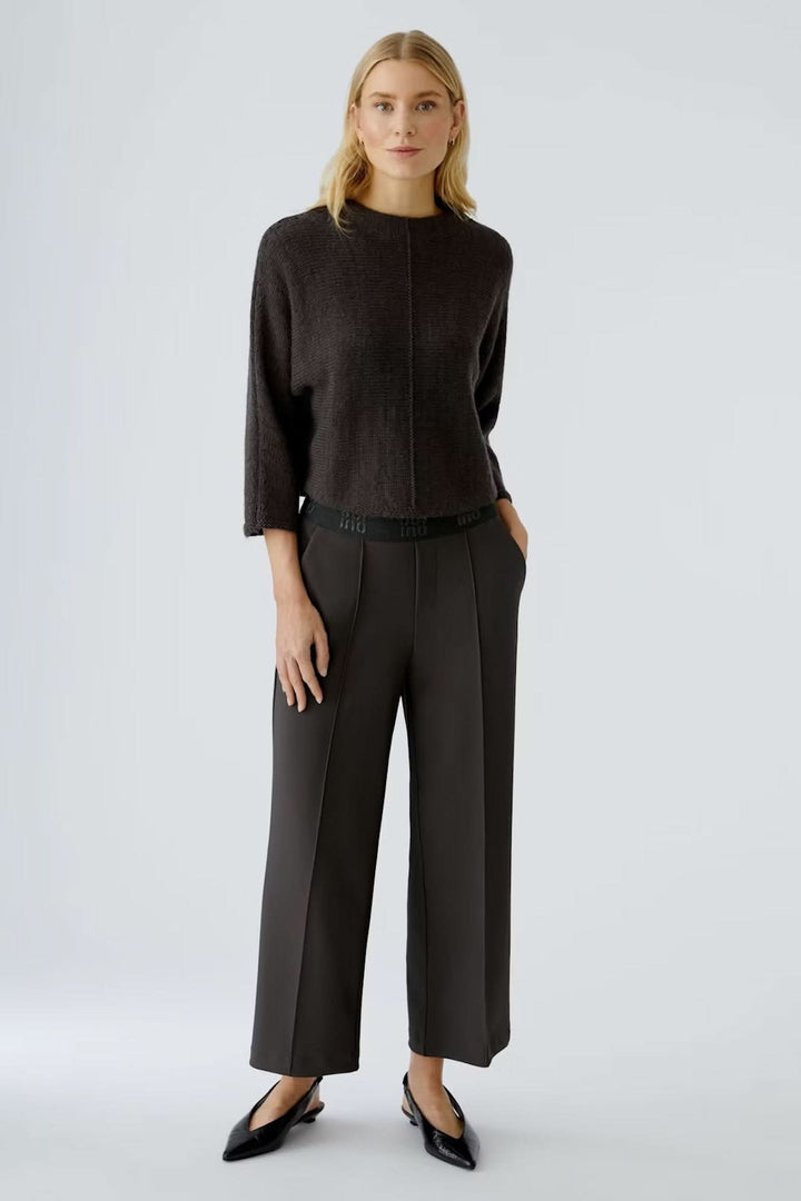 Femme portant un pantalon ample à taille élastique avec plis marqués, longueur cheville, élégance moderne et confort fluide.