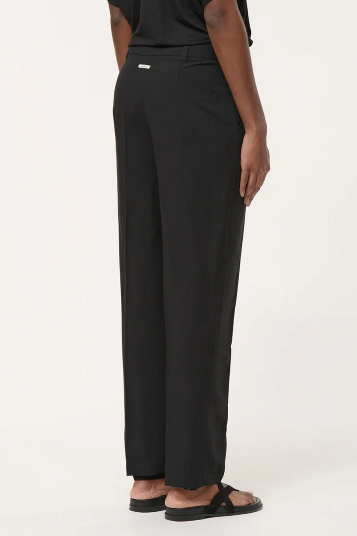 Personne portant un pantalon tailleur coupe droite noir élégant, vue de dos, illustrant la silhouette allongée et la ligne épurée.