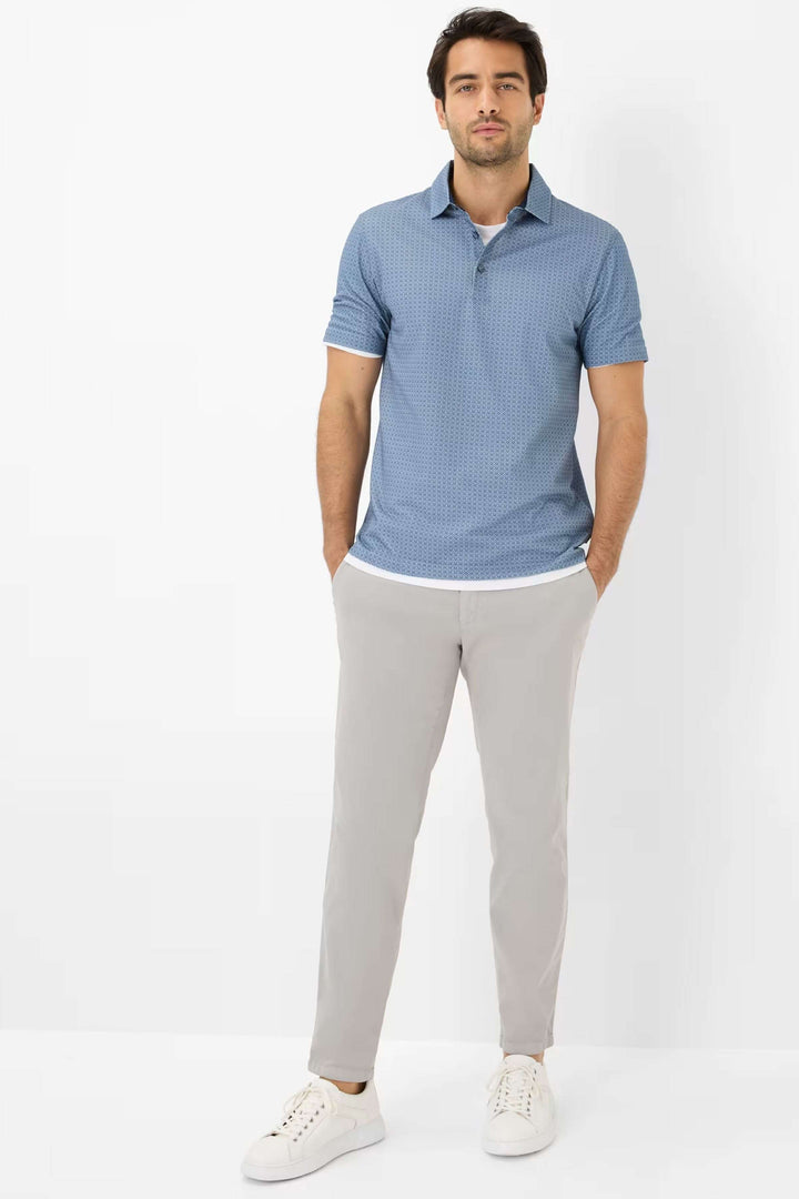 Homme portant un polo bleu en micro-motif avec des pantalons clairs, idéal pour un look décontracté chic.