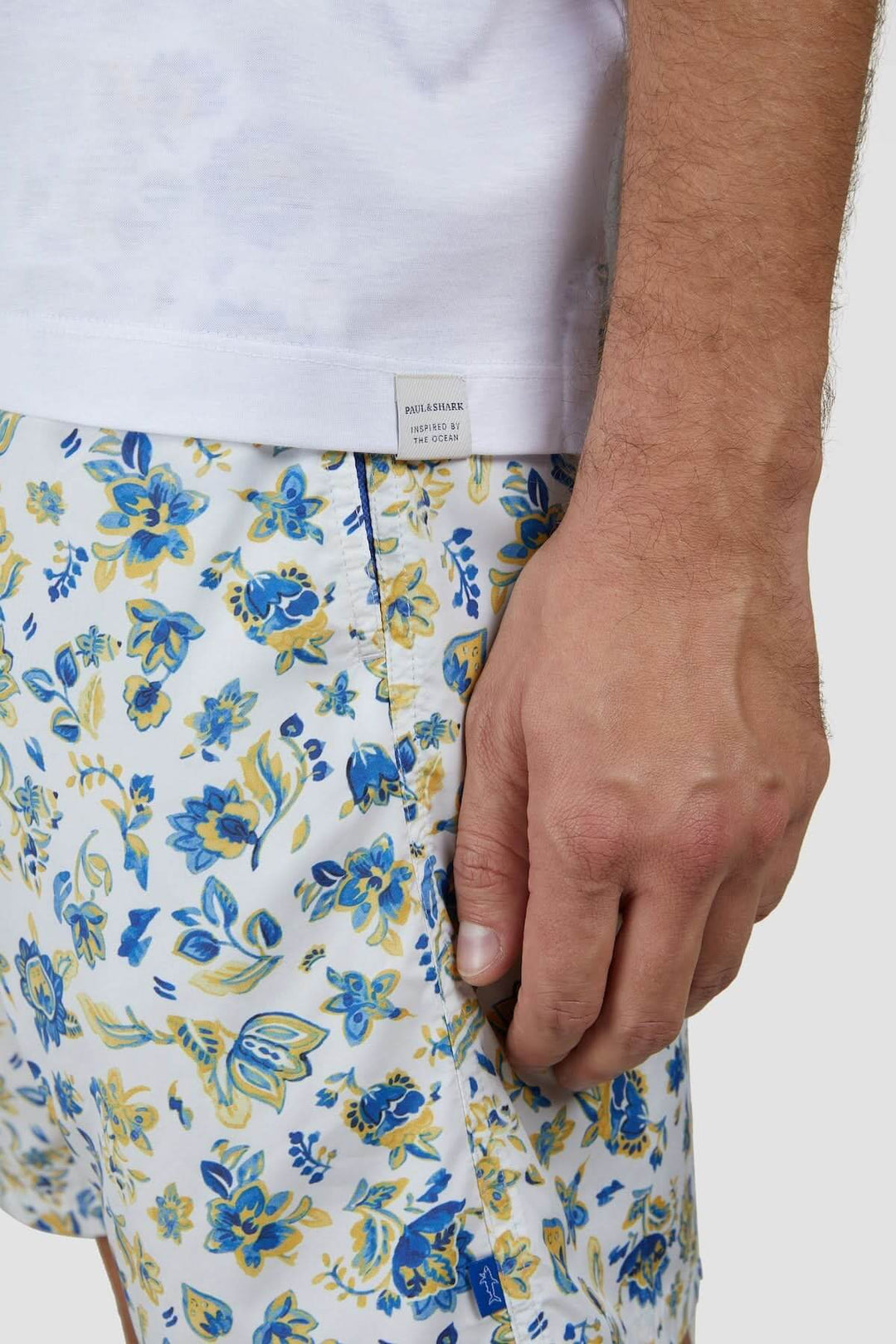 Homme portant un t-shirt blanc avec un short imprimé floral aux couleurs bleu et jaune.