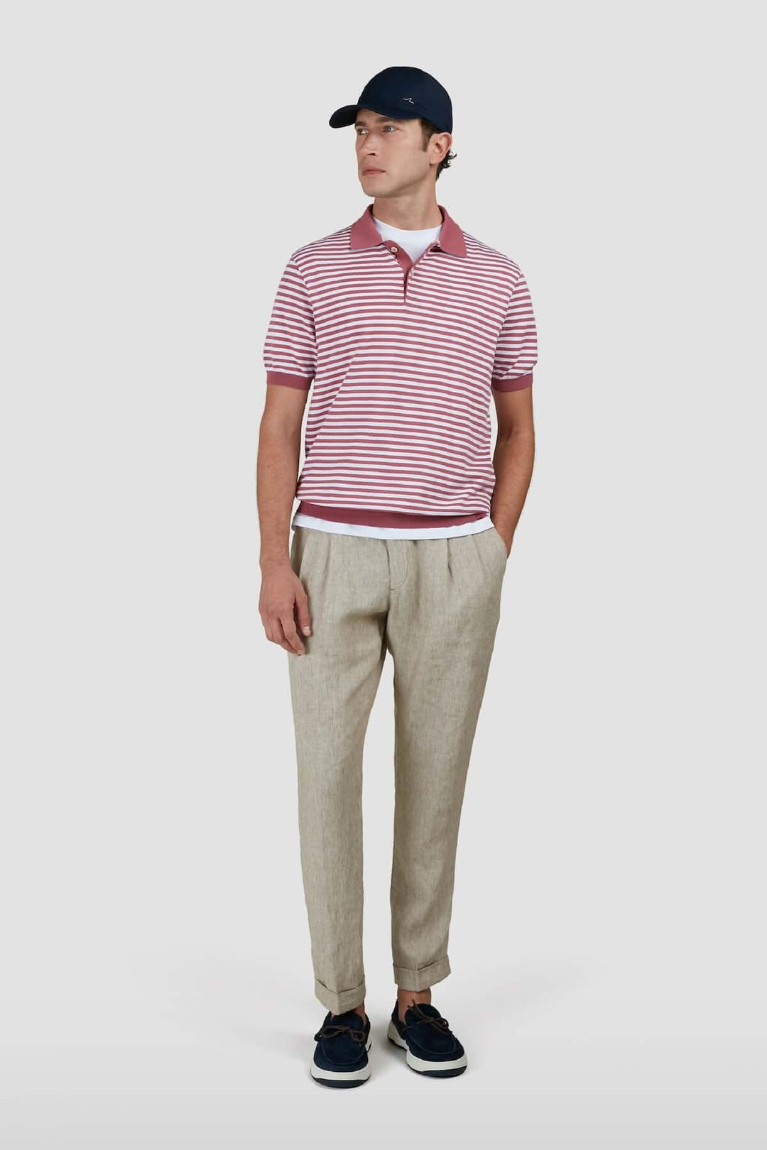 Homme portant un polo en coton à rayures rouges et blanches, avec pantalon et casquette marine.