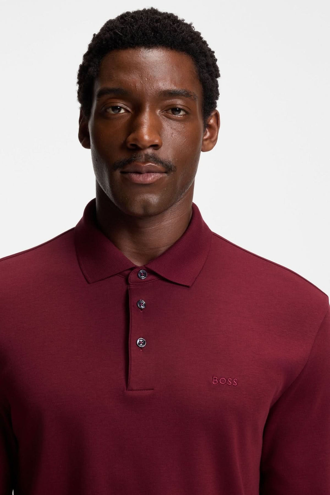 Homme portant un Polo manches longues Pado BOSS de couleur bordeaux avec col plat et patte à trois boutons.