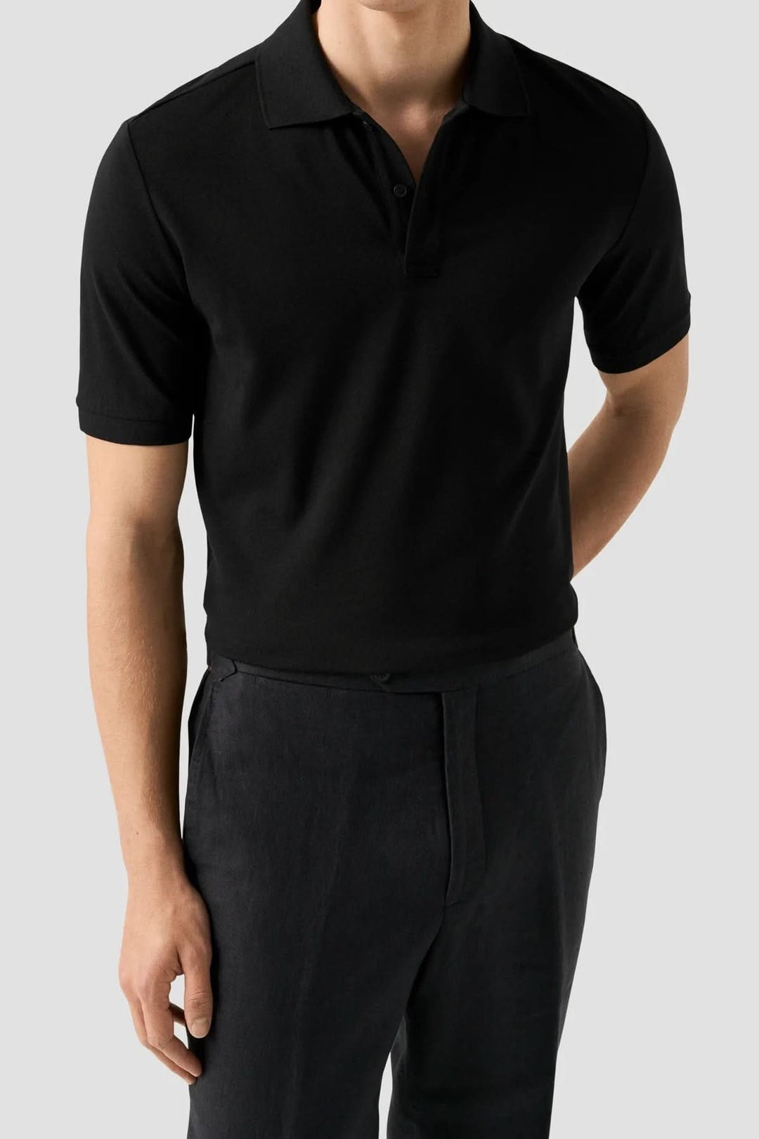 Homme portant un polo piqué à manches courtes noir, coupe ajustée et col structuré, intégrant un style moderne et polyvalent.