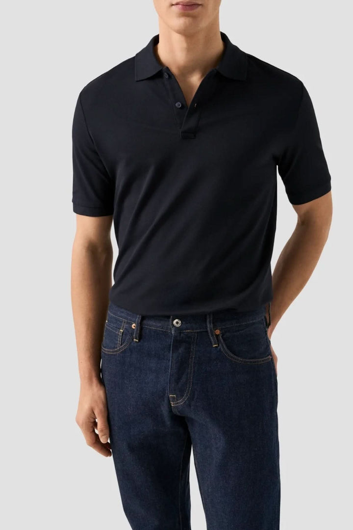 Homme portant un polo piqué à manches courtes ajusté, noir, avec col structuré, combiné avec un jean pour un style moderne et décontracté.