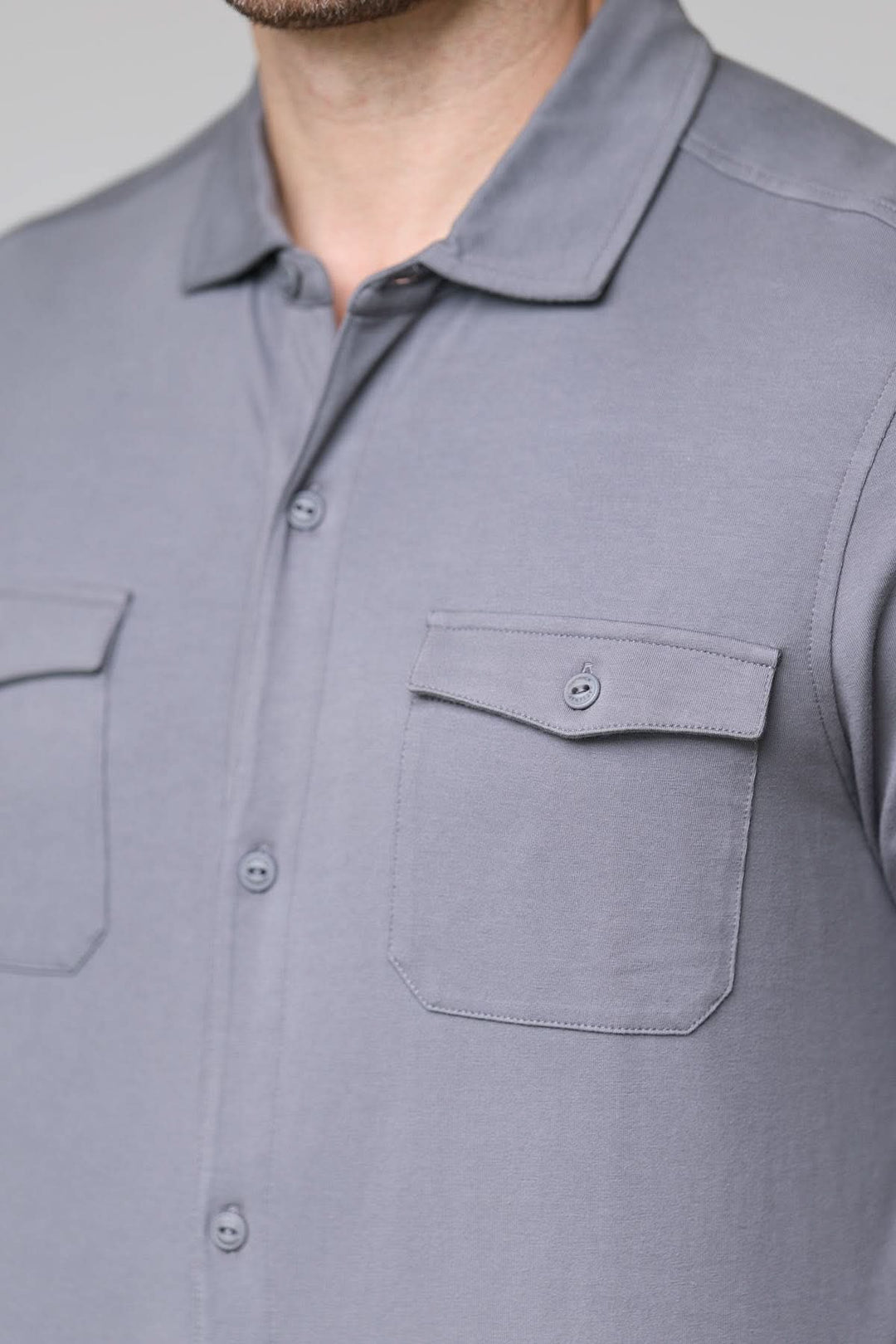 Polo à poches boutonnées gris avec col chemise, manches longues, et poches poitrine boutonnées, tissu doux et extensible.