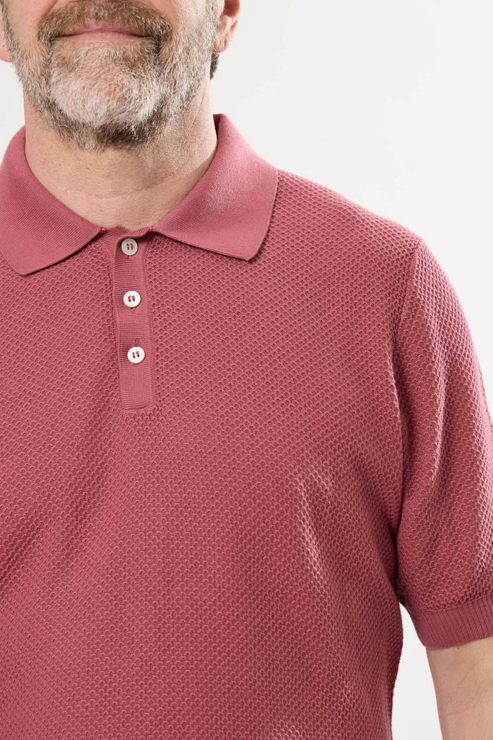 Homme portant un polo raffiné en maille texturée rose avec col structuré et boutons.
