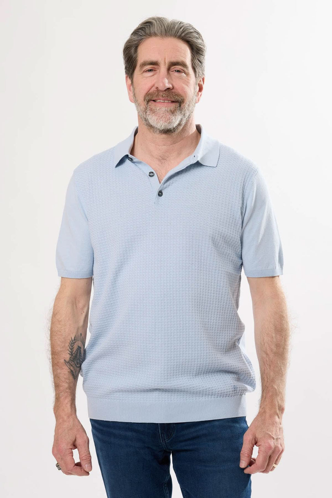 Homme souriant portant un polo rétro léger de couleur bleu, style élégant avec col classique et manches courtes.