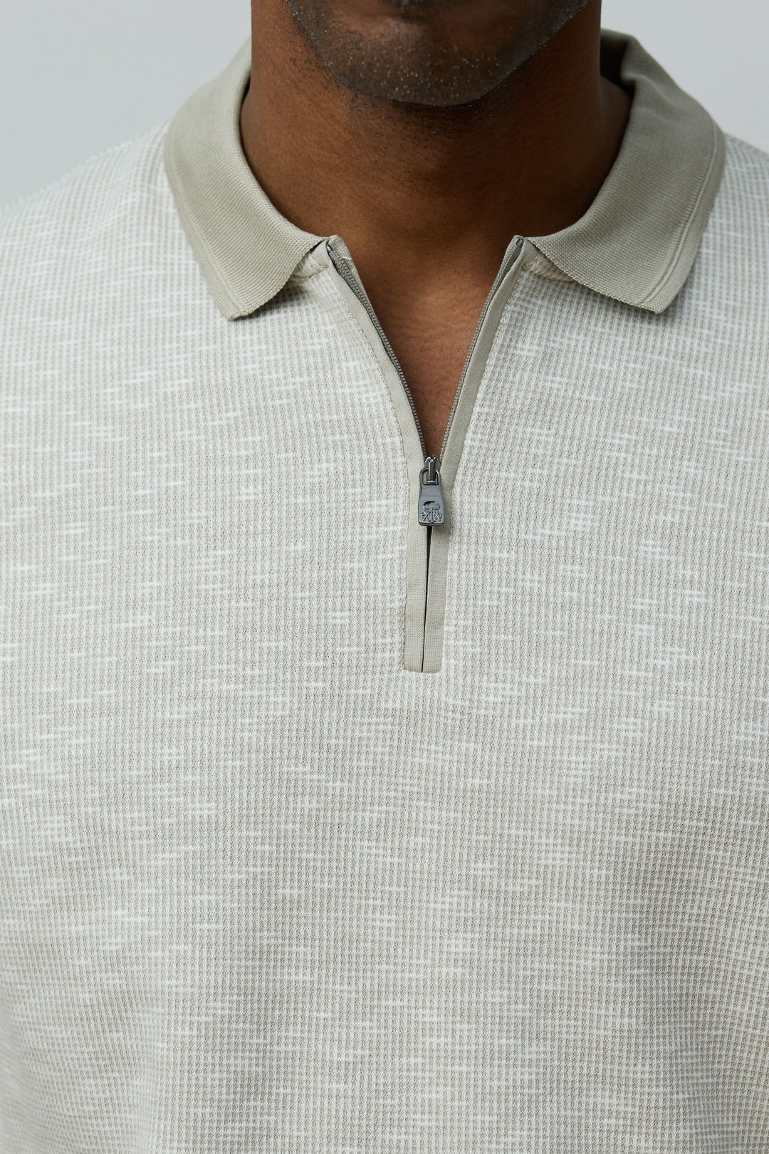 Homme portant un polo texturé à fermeture zippée en coton, style décontracté et raffiné.