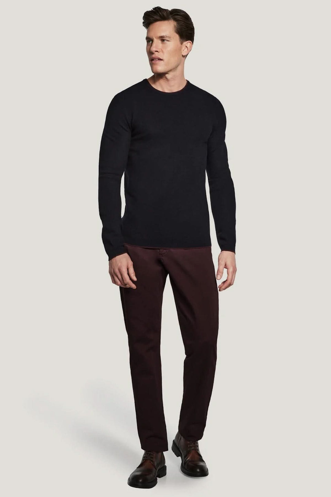 Homme portant un pull col ras du cou Belvedere en laine noir élégant, adapté sous une veste, avec un pantalon marron confortable.