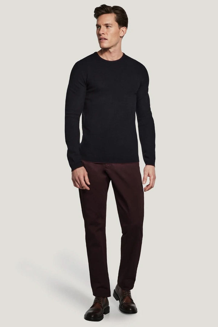 Homme portant un pull col ras du cou Belvedere en laine noir élégant, adapté sous une veste, avec un pantalon marron confortable.