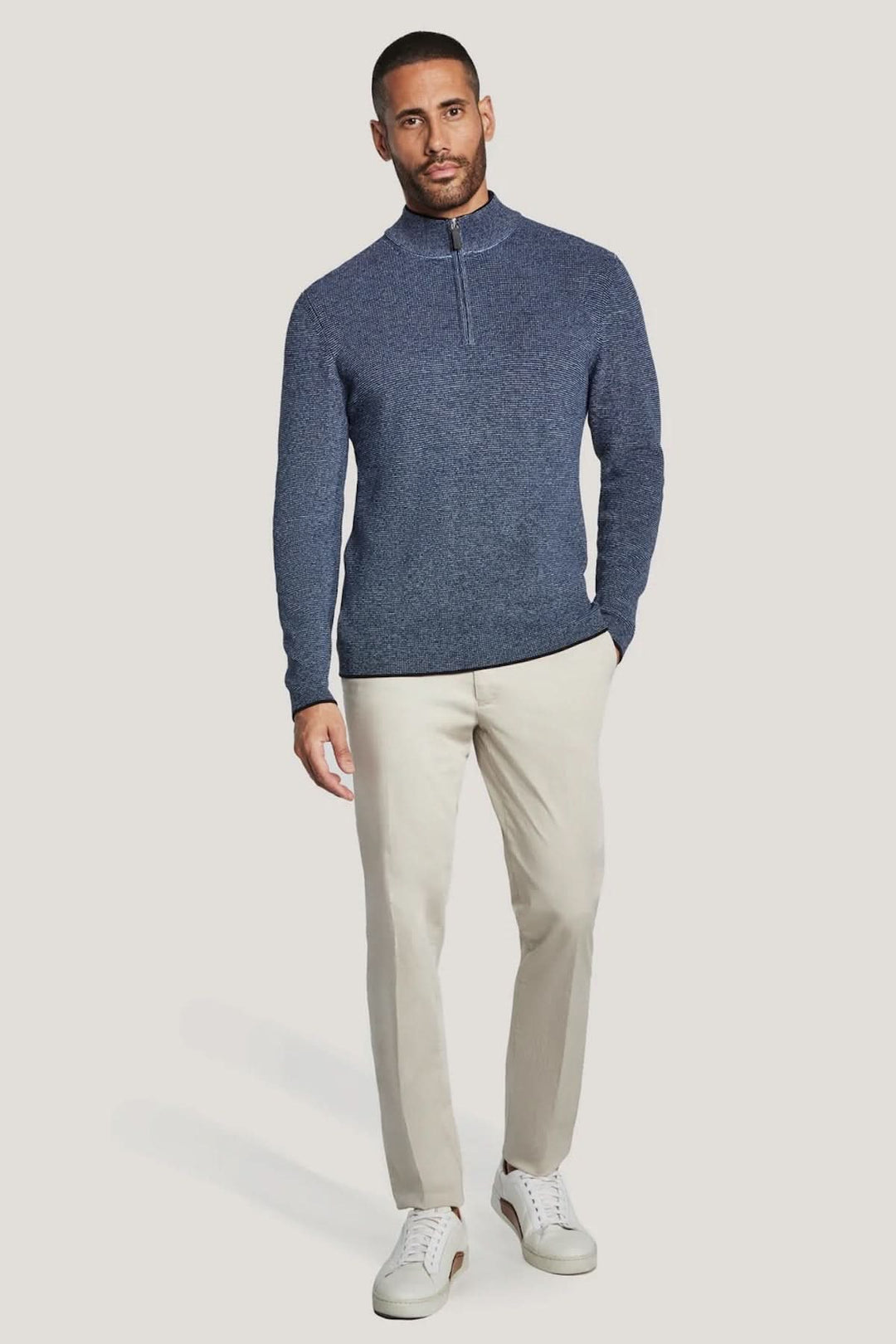 Homme portant un pull quart de zip en coton texturé bleu, avec un pantalon beige, style moderne et épuré.
