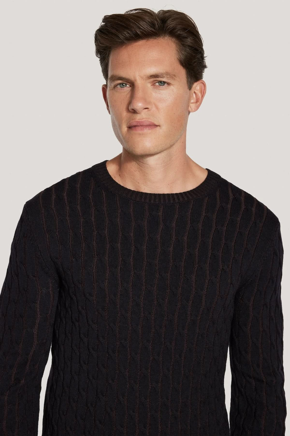 Homme portant un pull ras du cou torsadé en laine mérinos vanisée, noir, avec motif moderne et texture tricotée.