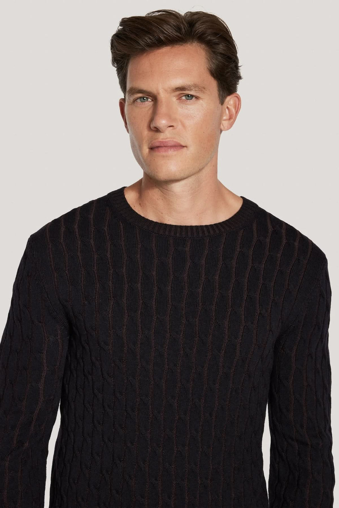 Homme portant un pull ras du cou torsadé en laine mérinos vanisée, noir, avec motif moderne et texture tricotée.