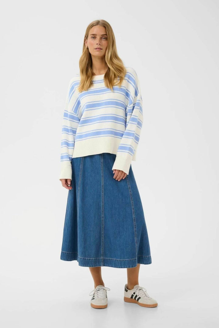 Modèle portant le Pull à rayures Serafine bleu et blanc, coupe droite ample, avec une jupe en jean et des baskets blanches.