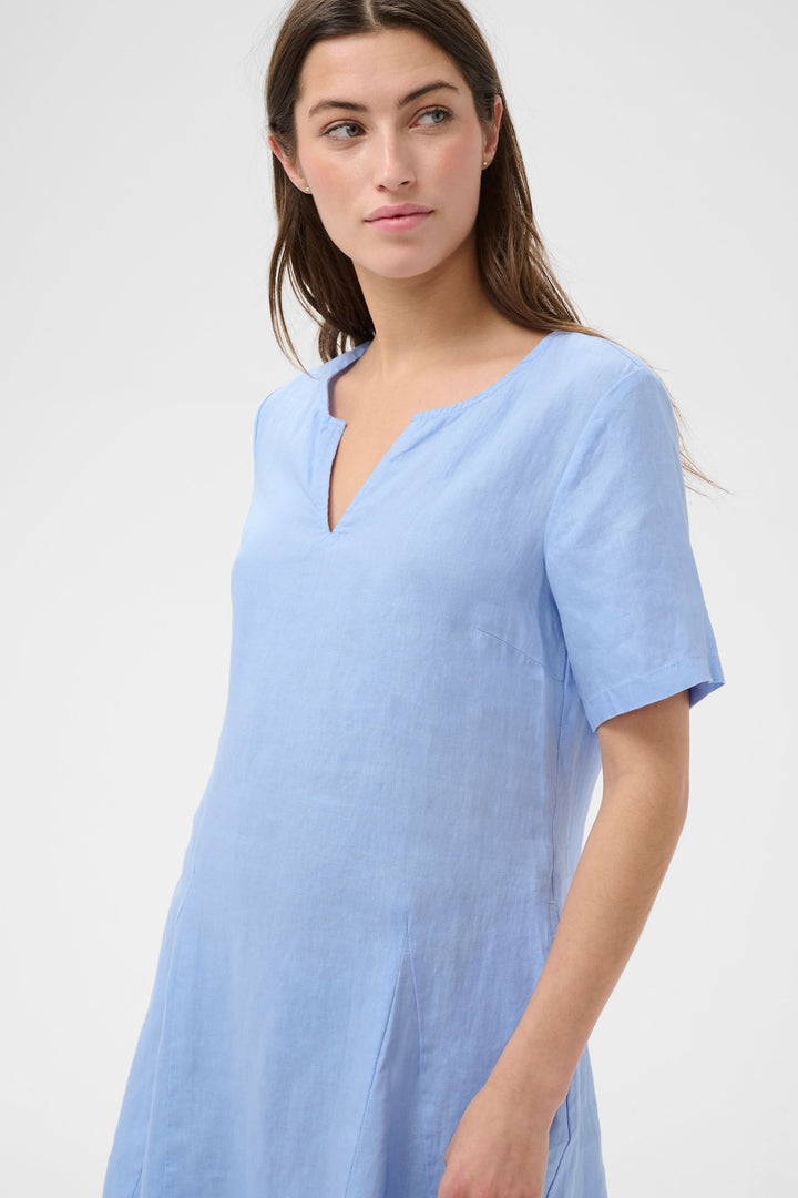 Robe Aminasa encolure en V, coupe fluide et élégante, idéale pour un look naturel et estival avec poches latérales. Robe épurée et chic.