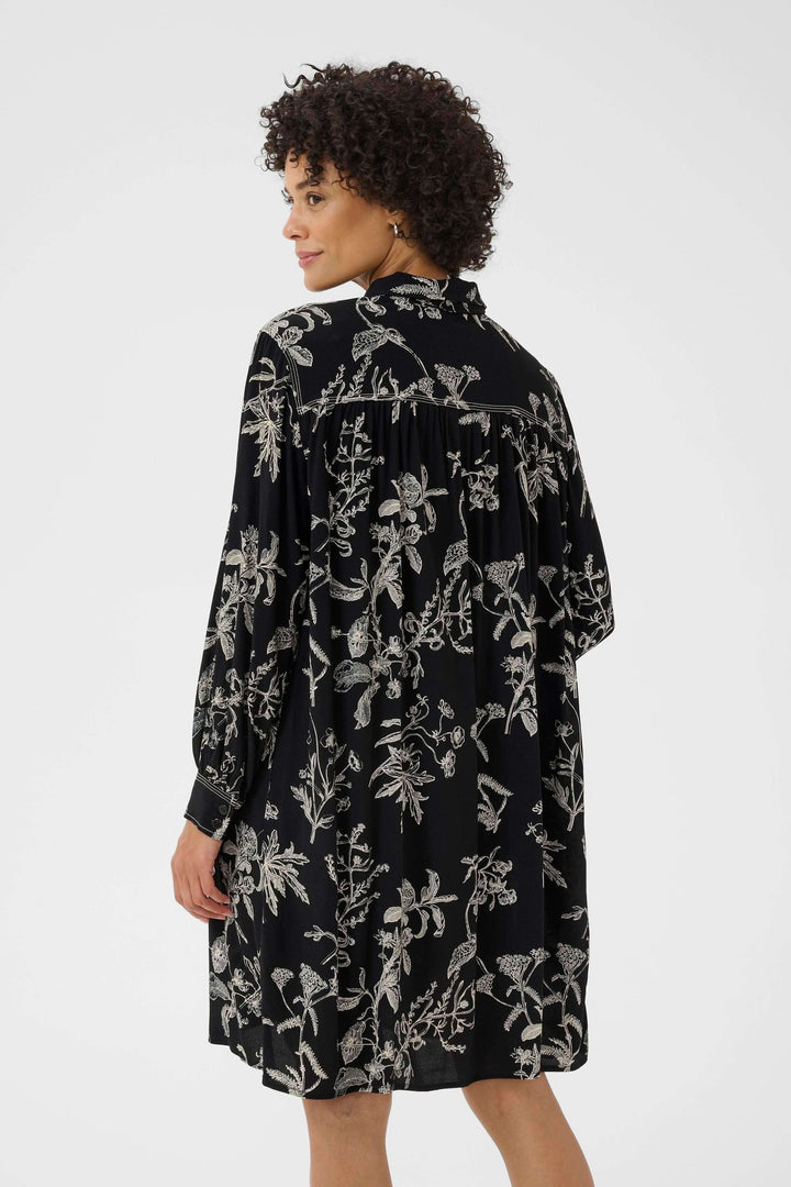 Femme portant la Robe Sanes florale avec col lavallière et manches longues bouffantes, vue arrière, style chic et confortable.