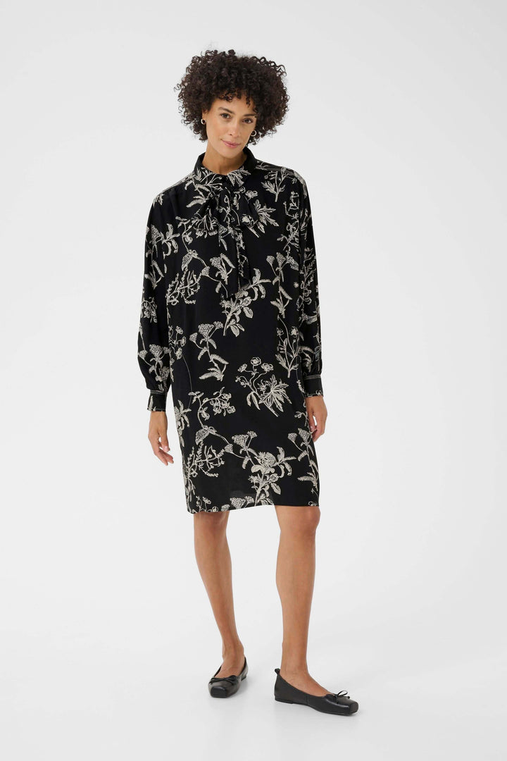 Femme portant une Robe Sanes noire à imprimé floral avec col lavallière et manches longues, style chic et féminin.