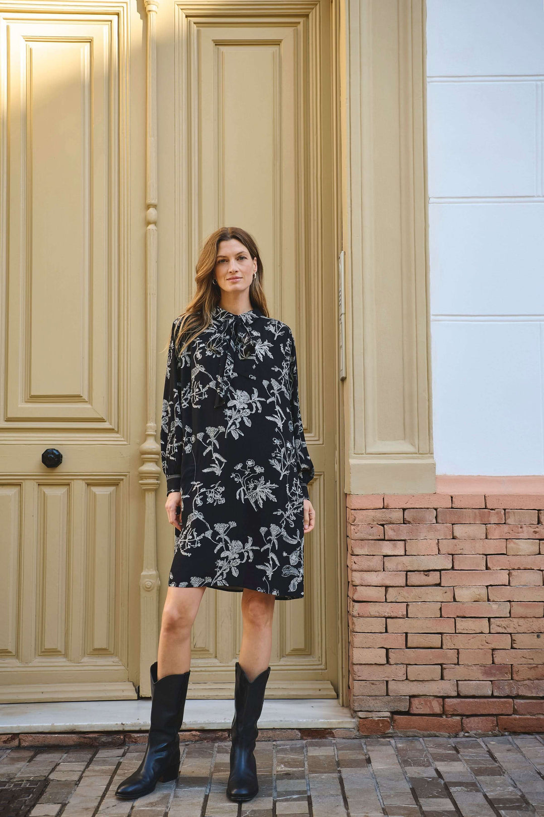 Robe Sanes à imprimé floral avec col lavallière et manches longues, portée avec des bottes pour un look chic et féminin.