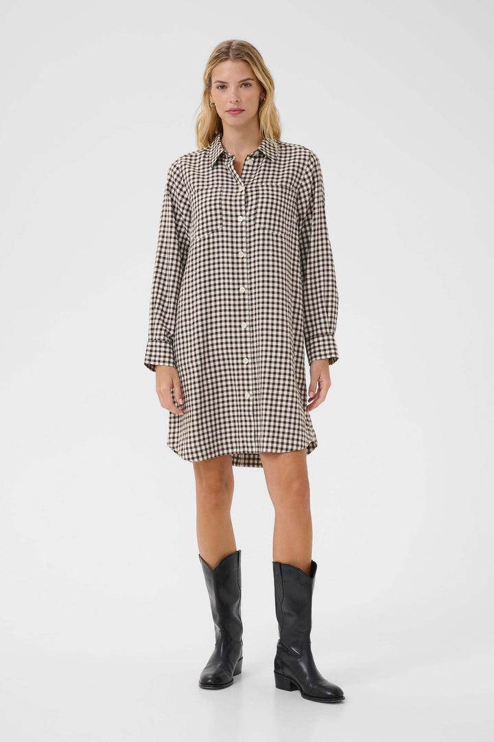 Femme portant la Robe Sardias à carreaux avec manches retroussables, style casual-chic avec des bottes noires.
