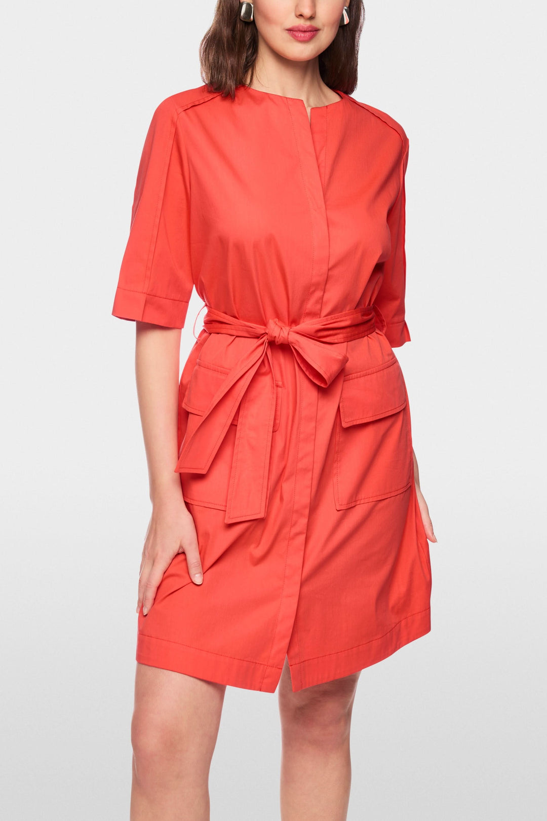 Femme portant une robe ceinturée à manches courtes rouge avec ceinture à nouer, design épuré et détails utilitaires.