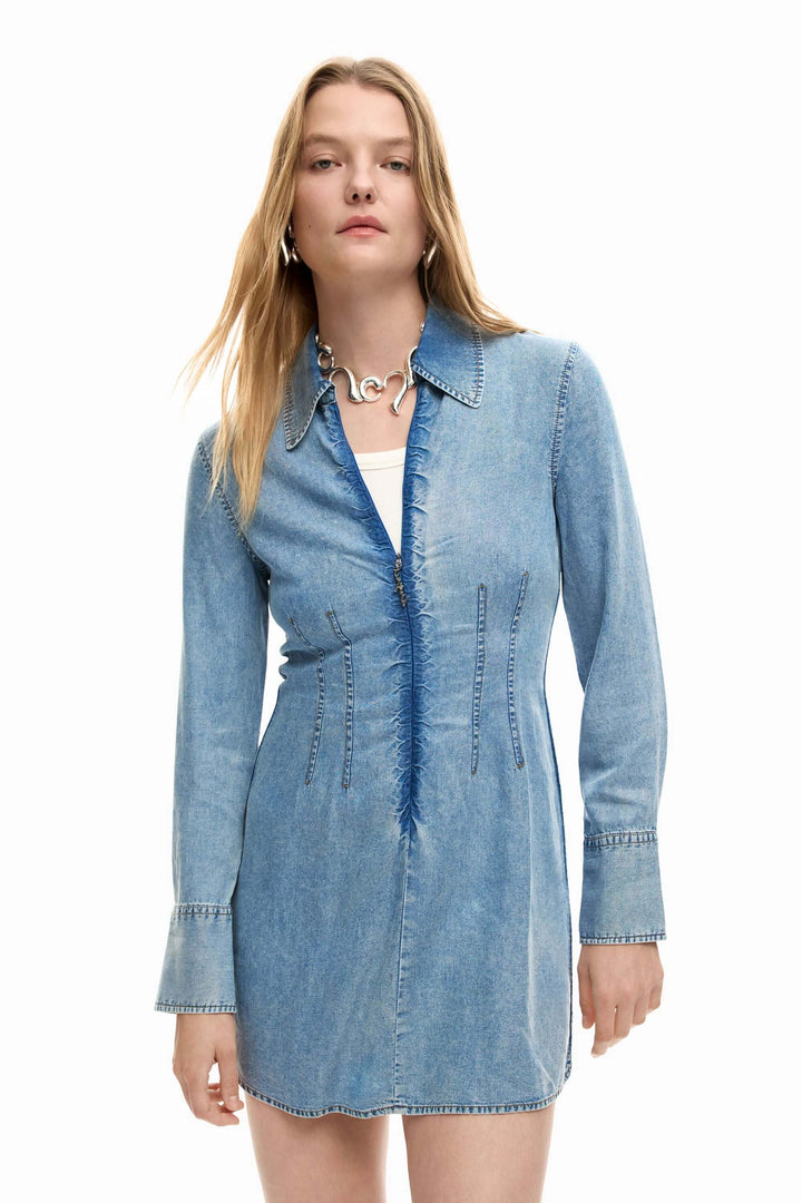 Femme portant une robe en jean slim avec des fronces et un col chemise, silhouette féminine et structurée.
