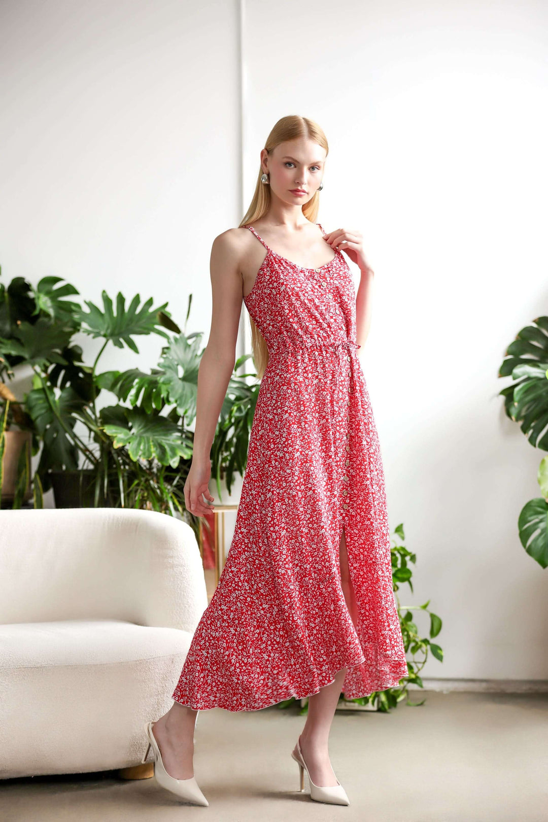 Robe fleurie fluide rouge à imprimé délicat, coupe évasée, bretelles fines, longueur midi, allure estivale, portée devant des plantes.