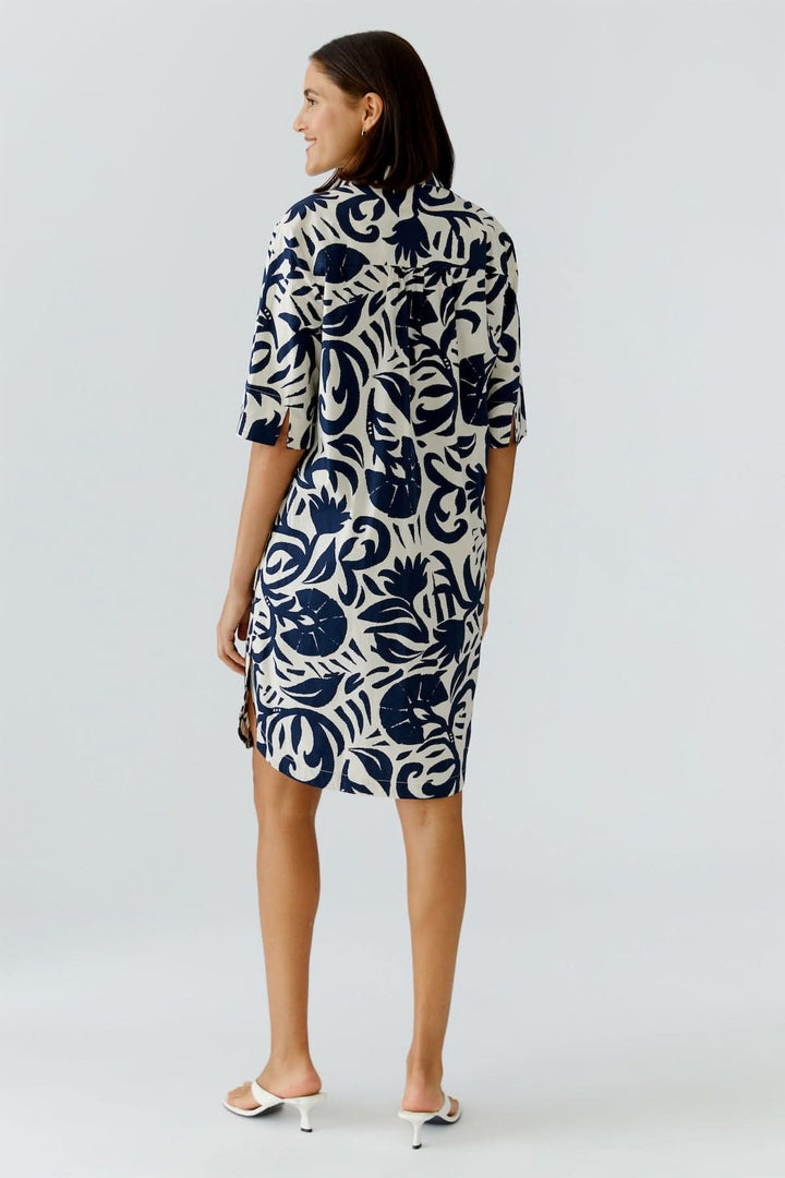 Femme portant une robe fluide à imprimé graphique, coupe droite, vue de dos, parfaite pour tenue décontractée ou habillée.