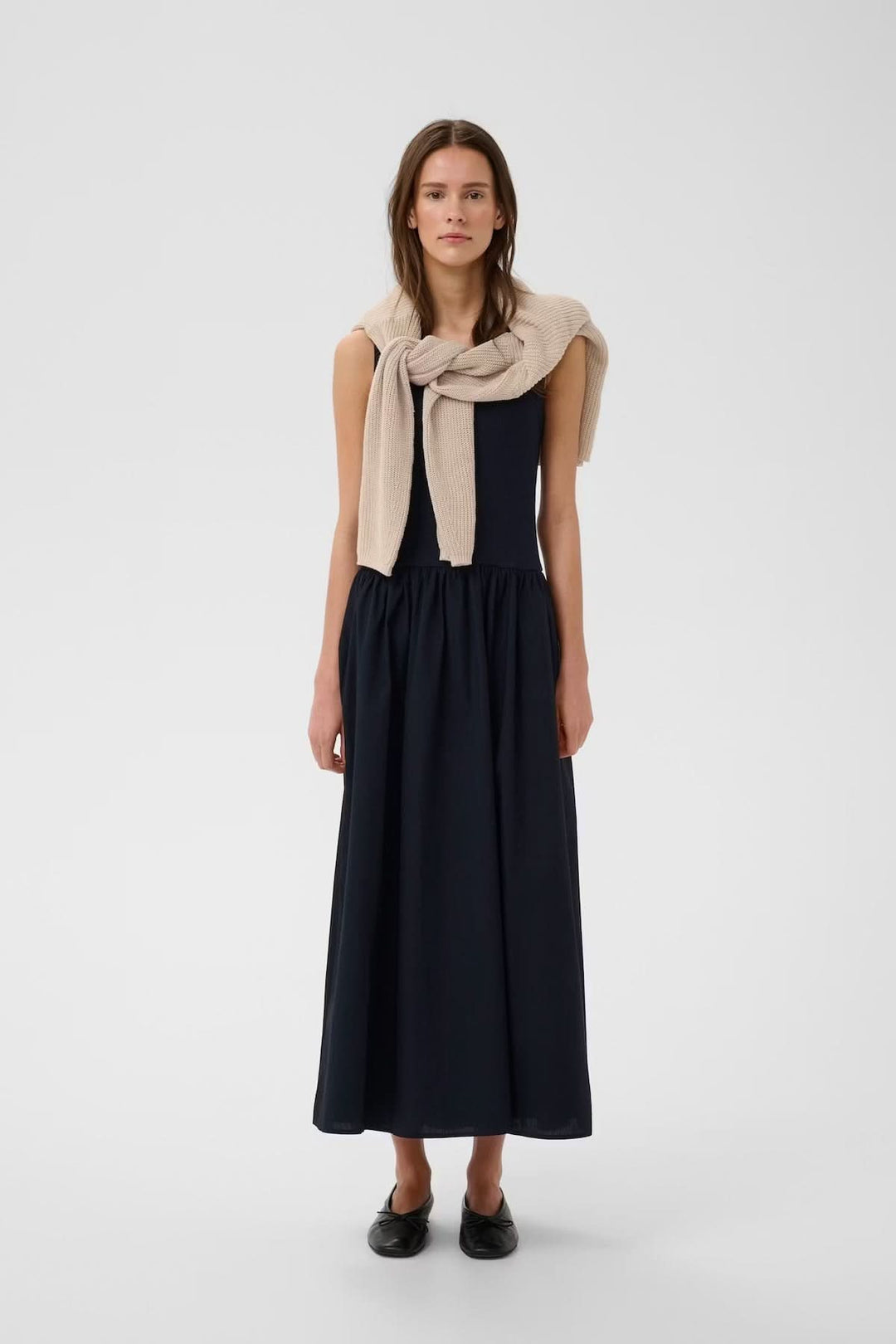 Femme portant la Robe midi sans manches Dagnama élégante, jupe ample et haut ajusté, mode raffinée et intemporelle.