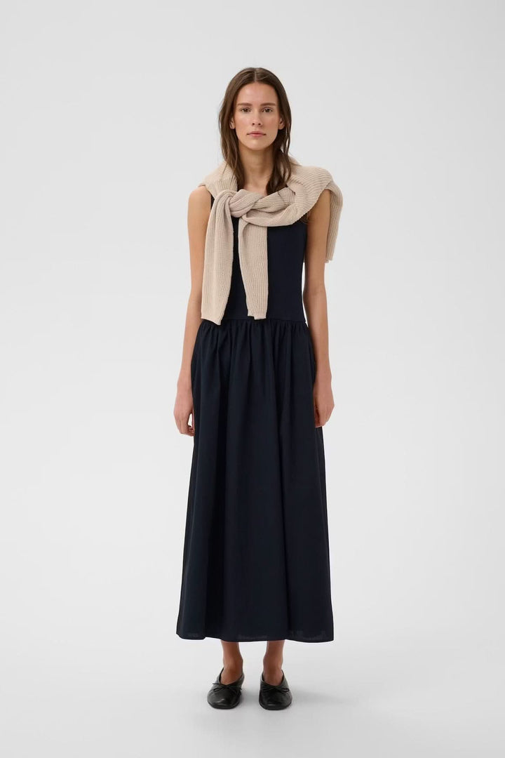 Femme portant la Robe midi sans manches Dagnama élégante, jupe ample et haut ajusté, mode raffinée et intemporelle.