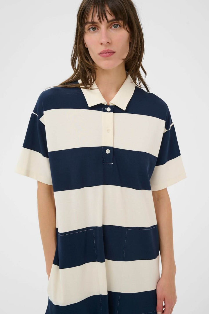Femme portant une robe polo Alise style sport chic avec bandes graphiques pour un look décontracté. Longueur midi, coupe droite, col polo.