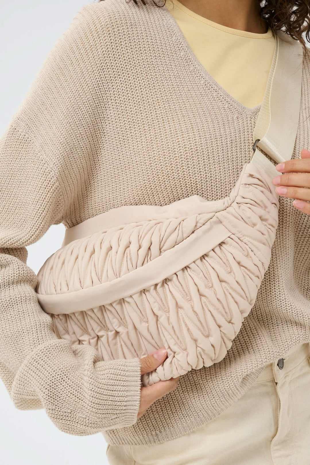 Femme portant un sac bandoulière matelassé Samy Bumbag beige avec texture froncée, ajustable et ergonomique, tenue décontractée.